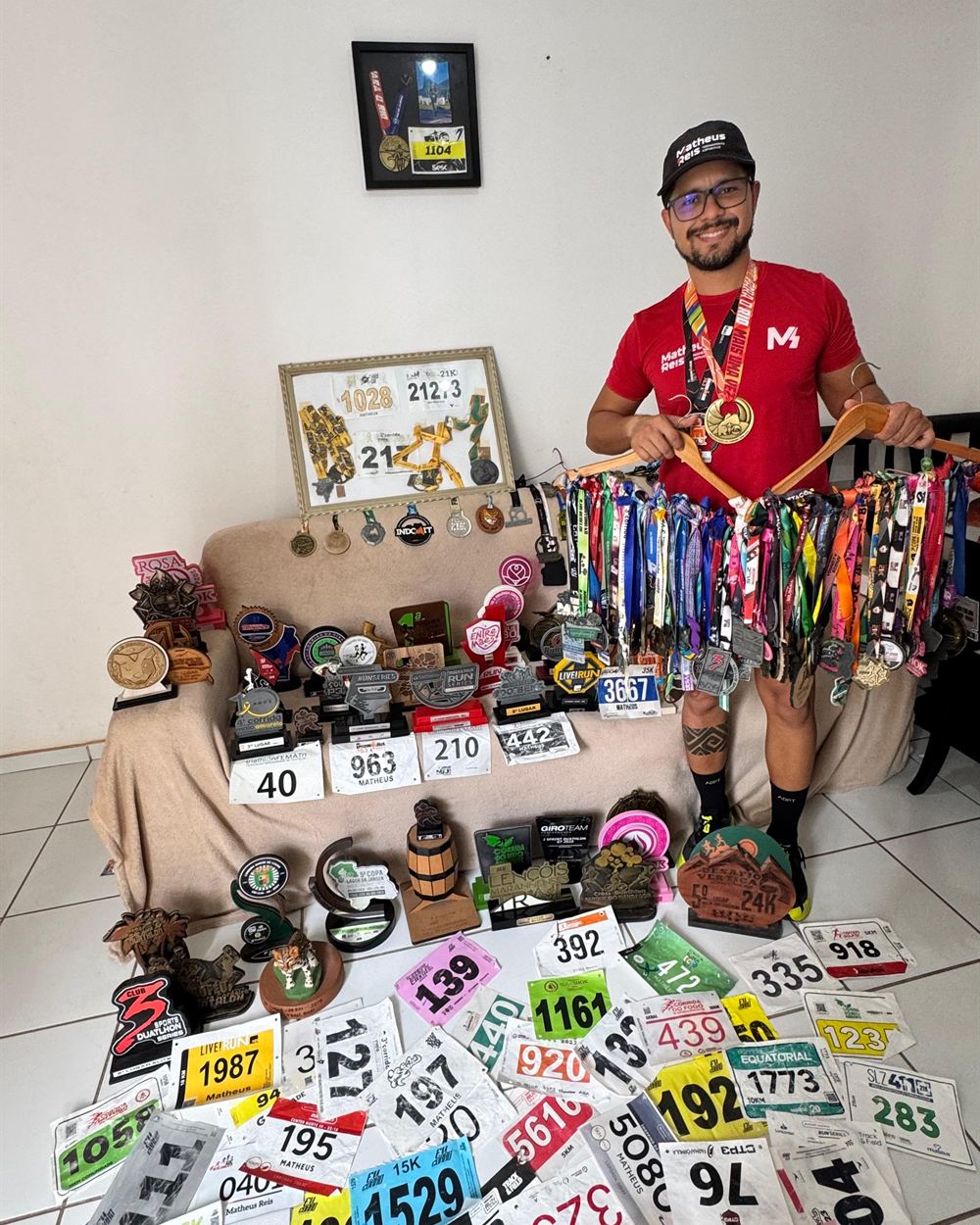 Matheus Reis com as medalhas, trofeus e numeros de peito das provas que disputou